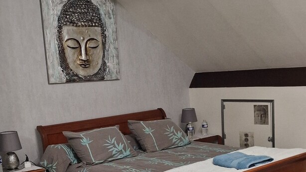 A bedroom with a wooden bed, a wall-mounted Buddha statue, a bedside table with a lamp, and a door with a poster. - "Buddha" Room—perfect for sporting events at the Le Mans circuit (Le Mans)