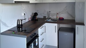 Une cuisine compacte avec des meubles blancs, un four encastré, un petit réfrigérateur et un plan de travail en bois.