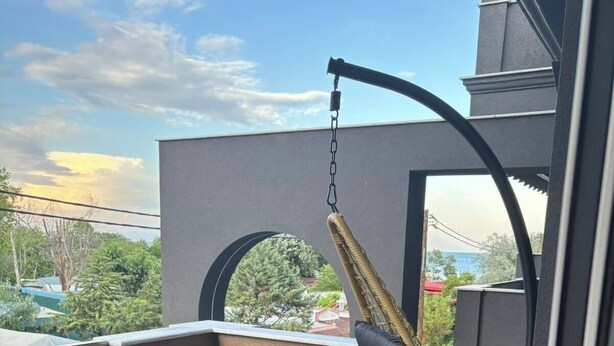 Un balcon avec un fauteuil suspendu, un fauteuil rembourré et une vue sur la mer et les bâtiments.