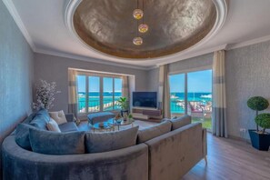 A living room with a curved sofa, a flat-screen TV, and a view of the ocean. - Marina Apartment Sea view (Hurghada)