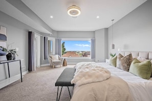 Ein modernes Schlafzimmer mit einem großen Bett, einer Bank, einem Sessel und Blick ins Freie.