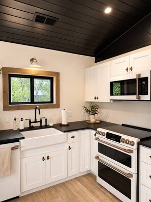 Una cocina moderna con armarios blancos, encimera negra, horno integrado y microondas.