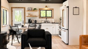 A modern kitchen with white cabinets, a black sofa, and a dining area with chairs. - The Cottage at Tongue River Canyon (Ranchester)