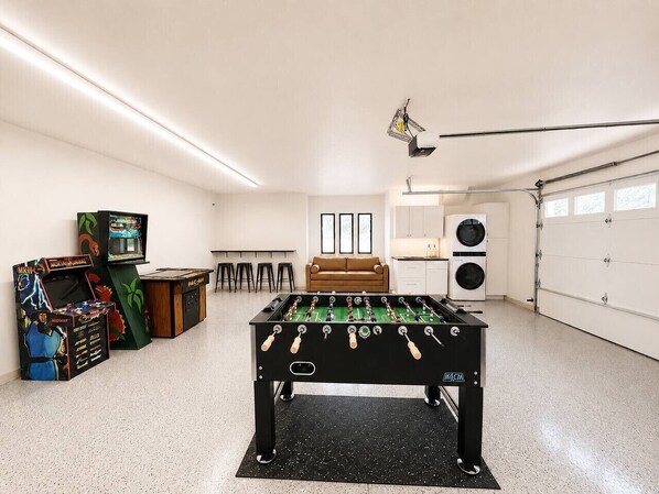 Una habitación con mesa de fútbol de mesa, mueble de futbolín, sofá, zona de cocina y garaje.