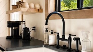 A kitchen with a black faucet, a coffee maker, and a window with a view of trees. - The Cottage at Tongue River Canyon (Ranchester)