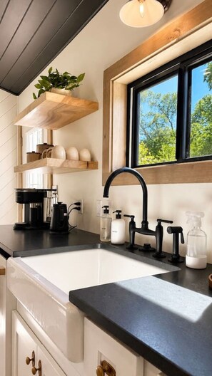 Eine Küche mit einem schwarzen Wasserhahn, einer Kaffeemaschine und einem Fenster mit Blick auf Bäume.