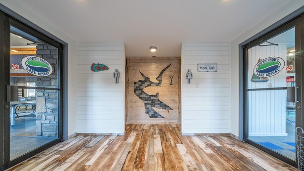 Ein Holzboden mit einer zentralen Mosaikwand, zwei Türen mit Hinweisschildern und einem Logo an den Wänden.