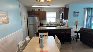 Una cocina equipada con refrigerador, microondas y estufa, una mesa de comedor con sillas, un sofá y una ventana con cortinas.