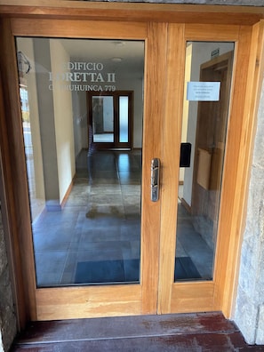 L’entrée d’un hôtel, avec une porte en bois et des panneaux de verre, un couloir au sol carrelé et une enseigne indiquant le nom et l’adresse du bâtiment.