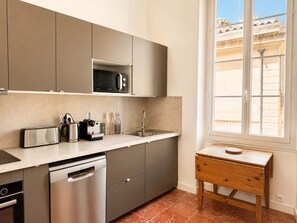 Eine moderne Küche mit Einbau-Mikrowelle, Toaster, Kaffeemaschine und Geschirrspüler. Ein Fenster bietet Blick auf umliegende Gebäude.