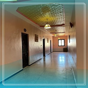Un largo pasillo con techo estampado, una puerta a la izquierda y una ventana a la derecha.