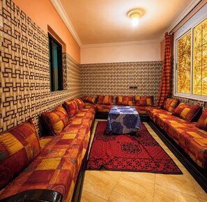 Um quarto com paredes estampadas, um sofá comprido, uma mesa pequena e uma janela com cortinas.