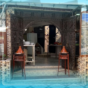 An entrance with intricate metalwork, a tiled floor, and a kitchen area visible through an open door.
