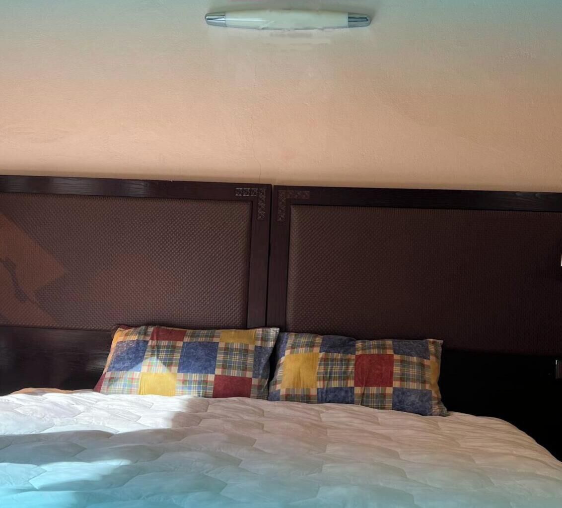 A bed with a quilt, two pillows with a plaid pattern, and a headboard with a textured design.