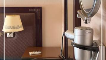 A hotel room with a bed, a bedside lamp, a hairdryer, a mirror, and a sign indicating international warranty service.