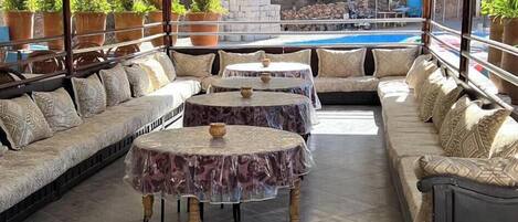 An outdoor seating area with cushioned sofas, round tables, and potted plants.