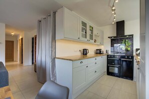 A modern kitchen with light-colored cabinets, a black stove, and a countertop with a coffee maker. - Marmottes 3-Bed, 2-Bath - Walk to Spa & Village (Saint-Gervais-les-Bains)