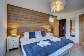 A bedroom with a wooden headboard, a bed with white bedding, two bedside tables with lamps, and a large mirror on the wall. - Marmottes 3-Bed, 2-Bath - Walk to Spa & Village (Saint-Gervais-les-Bains)