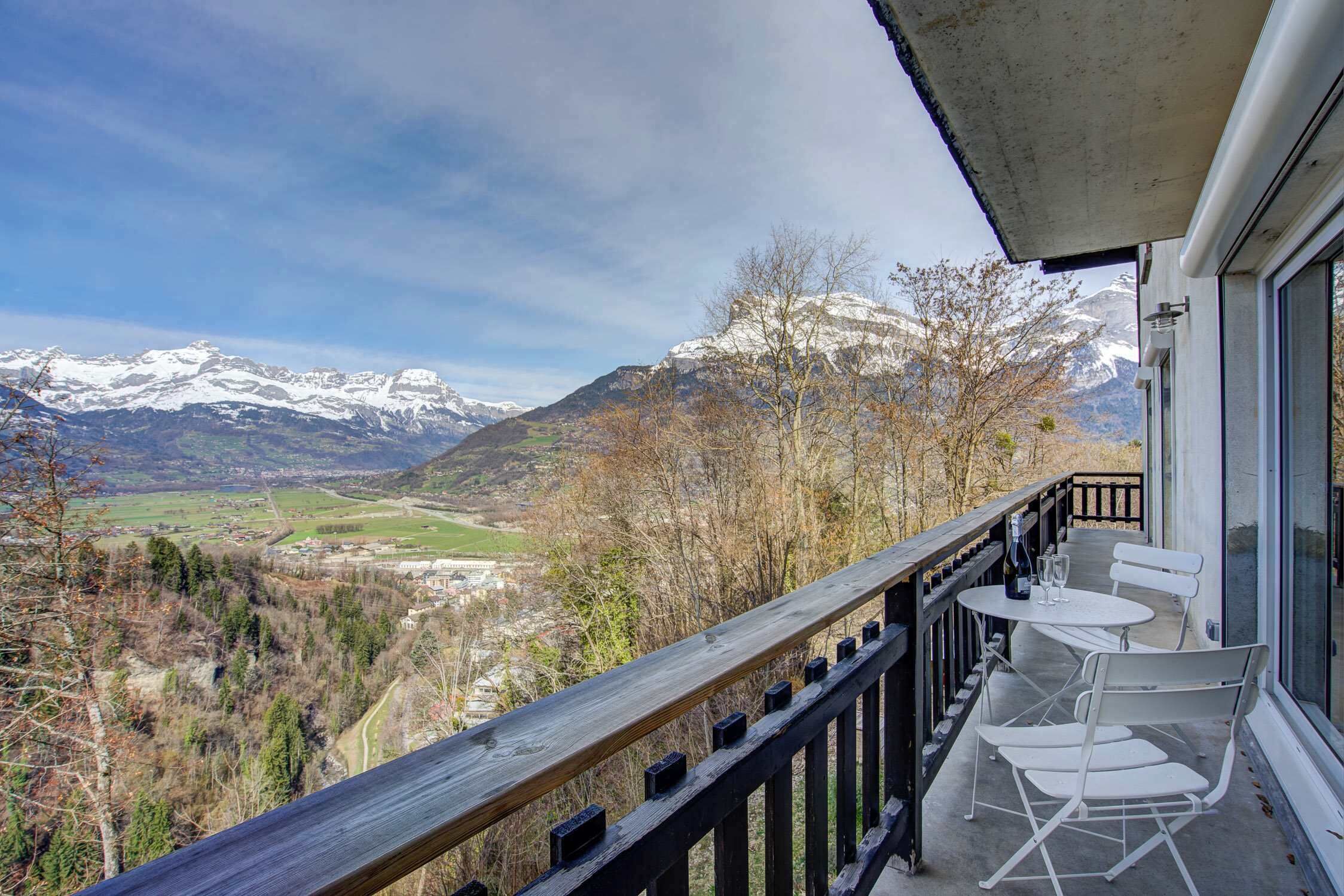 Ein Balkon mit Blick auf schneebedeckte Berge, einem Holgitter und einem Tisch mit Stühlen.