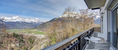 Un balcon offrant une vue sur des montagnes enneigées, avec une balustrade en bois et une table entourée de chaises.