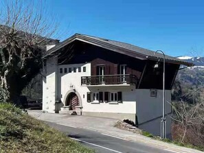 A two-story building with a balcony, a door with an arch, and a mountain in the background. - Marmottes 3-Bed, 2-Bath - Walk to Spa & Village (Saint-Gervais-les-Bains)
