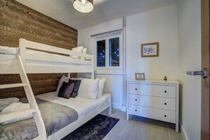 A bunk bed with a wooden headboard, a bedside table with drawers, a window with a view, and a framed picture on the wall. - Marmottes 3-Bed, 2-Bath - Walk to Spa & Village (Saint-Gervais-les-Bains)