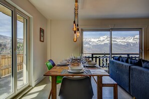 A dining area with a table set for four, a sofa, and a view of snow-capped mountains. - Marmottes 3-Bed, 2-Bath - Walk to Spa & Village (Saint-Gervais-les-Bains)