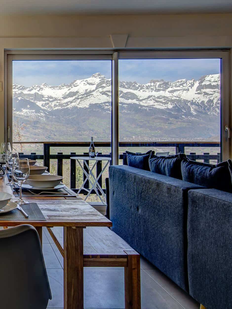 Habitación con un amplio ventanal que ofrece vistas a la montaña, un sofá, una mesa de comedor con sillas y una pequeña mesita auxiliar.