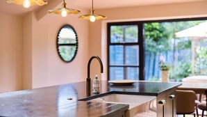 Cucina dal design moderno, con un'ampia isola dotata di lavello, rubinetto e dispenser di sapone. Sopra l'isola, lampade a sospensione e una finestra che offre vista sull'esterno.