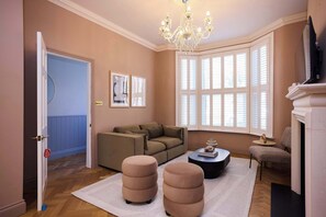 Ein Wohnzimmer mit einer Couch, Poufs, einem Couchtisch, einer Kristallleuchtre und einem Kamin.