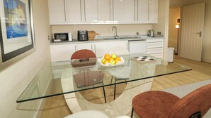 A modern kitchen with white cabinets, a glass dining table, and a bowl of fruit. - Suite 33B (Londonderry)