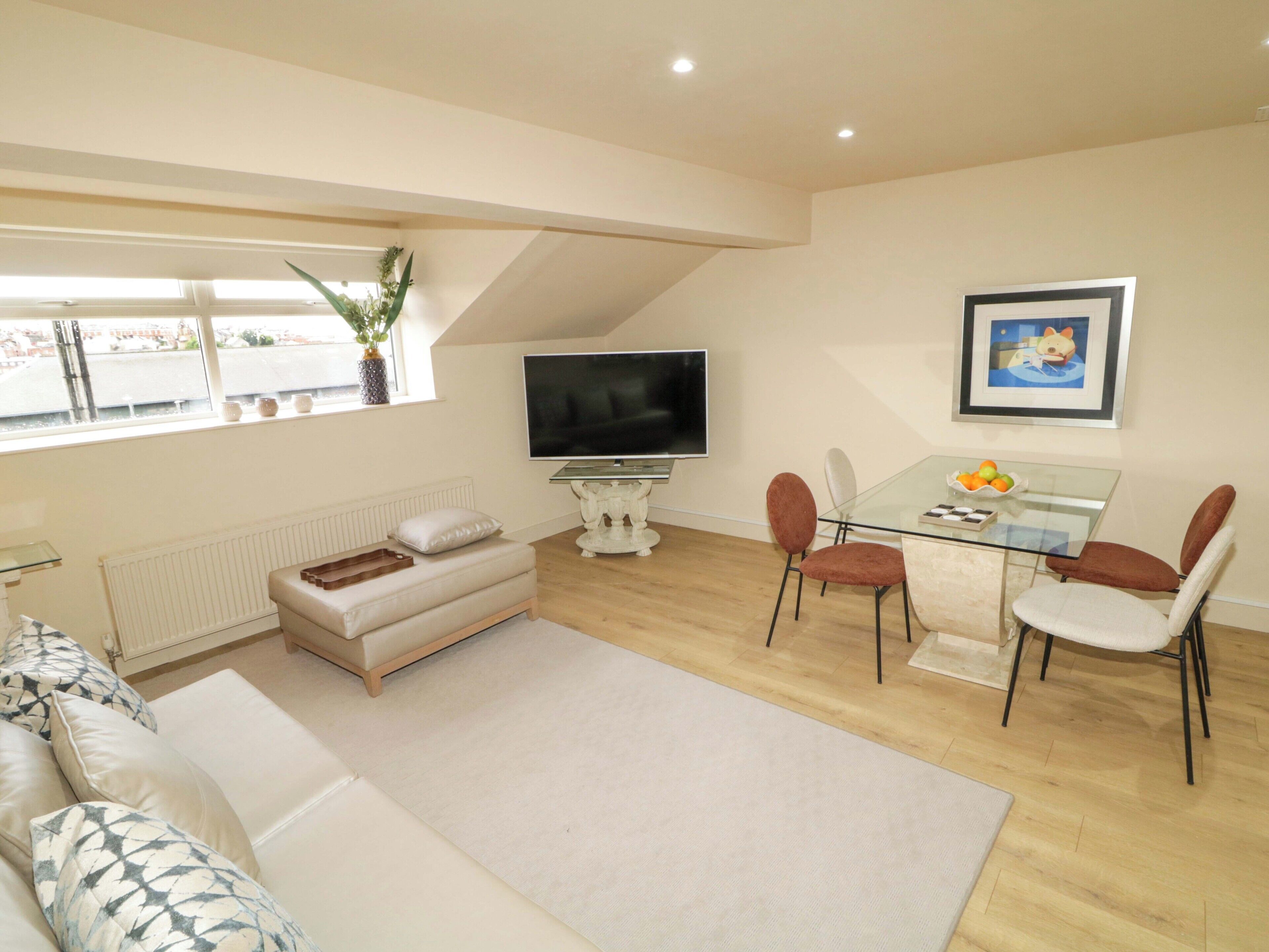 A living room with a sofa, TV, dining table, chairs, and a window with a plant.