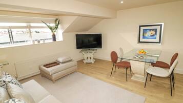 A living room with a sofa, TV, dining table, chairs, and a window with a plant.