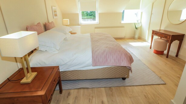 A bedroom with a bed, bedside table, lamp, dresser, radiator, window, and a mirror. - Suite 33B (Londonderry)