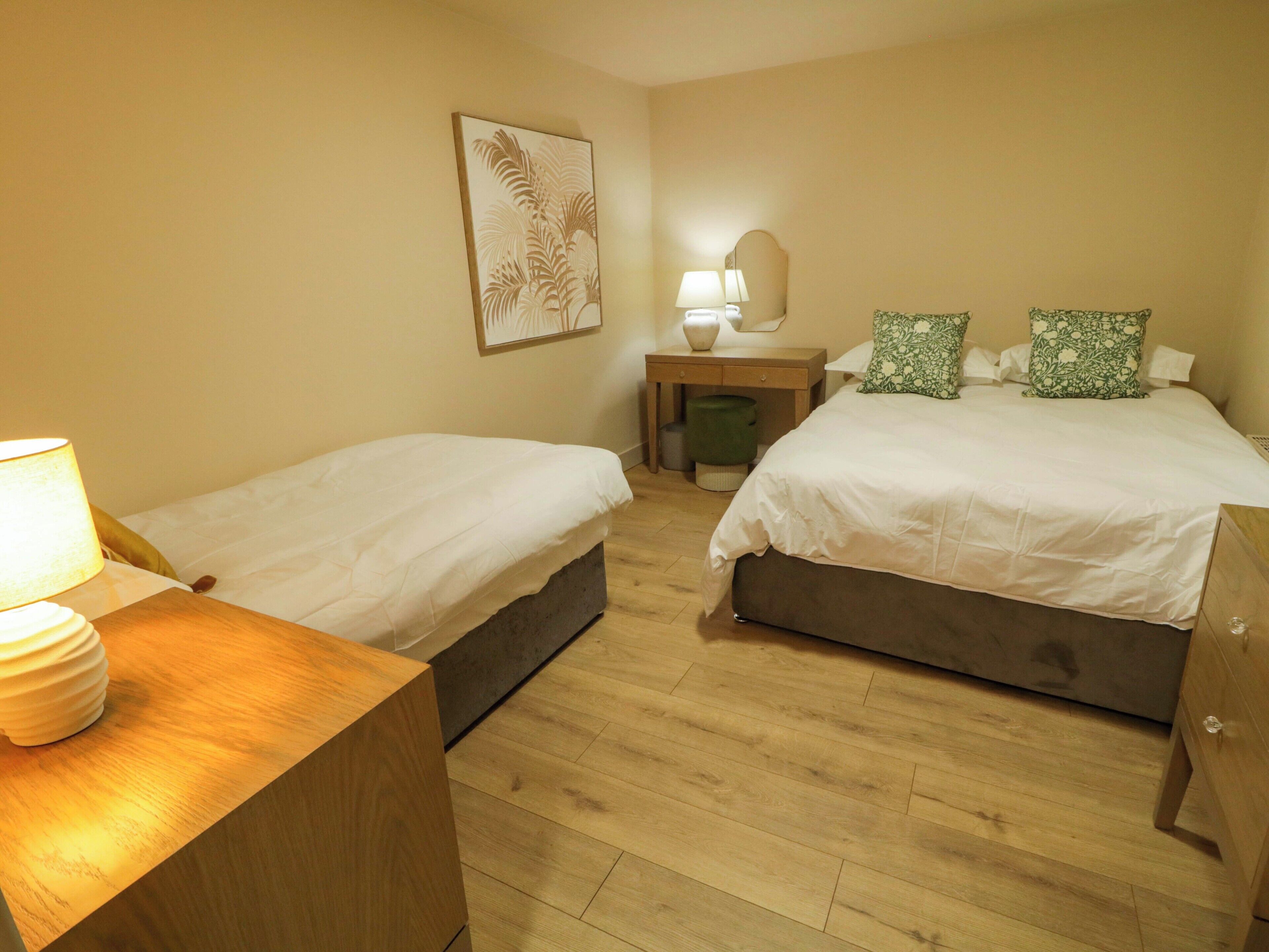 Een hotelkamer met twee eenpersoonsbedden, een houten nachtkastje met een lamp, een bureau met een spiegel en een kamerplant in een lijst aan de muur.
