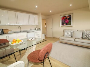 A modern kitchen with white cabinets, a glass dining table, and a red chair. - Suite 33B (Londonderry)