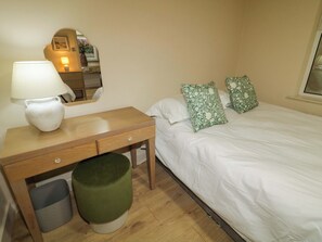 A bedroom with a wooden desk, a green ottoman, a white bed with green floral pillows, and a mirror on the wall. - Suite 33B (Londonderry)