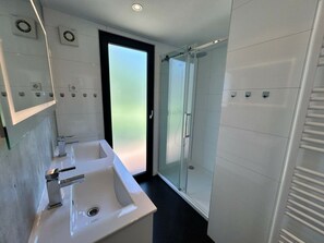 Ein modernes Badezimmer mit zwei Waschbecken, einer Duschkabine aus Glas und einer Tür mit Milchglas.