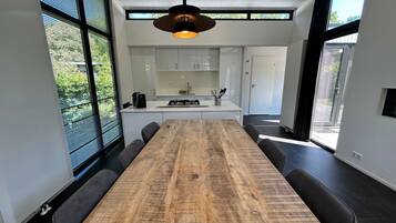A modern kitchen with white cabinets, a wooden dining table, and a hanging light fixture.