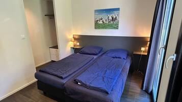 A bedroom with a bed, bedside tables, a nightstand, a painting, and a door.
