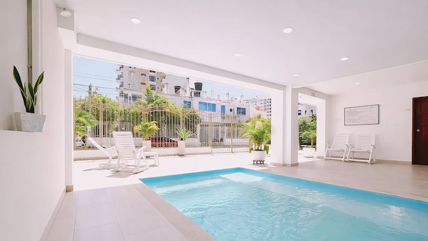 En modern inomhuspool med fri utsikt över stadsbilden, vita kakelplattor på golvet och några krukväxter.