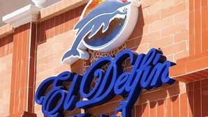 En hotellskylt med en delfinlogotyp och namnet ”El Delfino Hotel” skrivet med blå bokstäver.