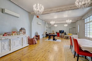 Ein geräumiges Zimmer mit Holzboden, einer Essecke mit Tisch und Stühlen, einem Fernseher und einer Kristallleuchter.
