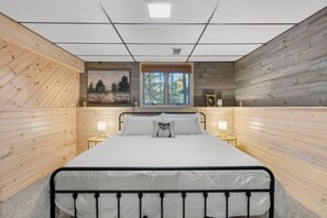 Quarto com cama, duas mesas de cabeceira, uma janela e paredes de madeira.