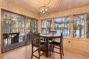 Una habitación con paneles de madera, una mesa de comedor y sillas, ventanas grandes y vistas a un bosque nevado.