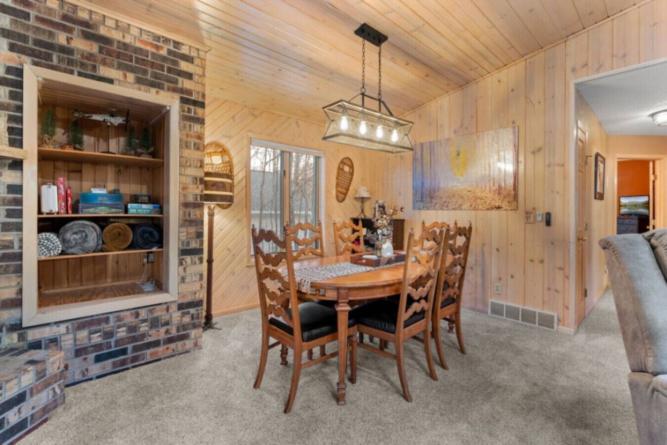 A dining area with a brick wall, wooden dining table, chairs, and a hanging light fixture.