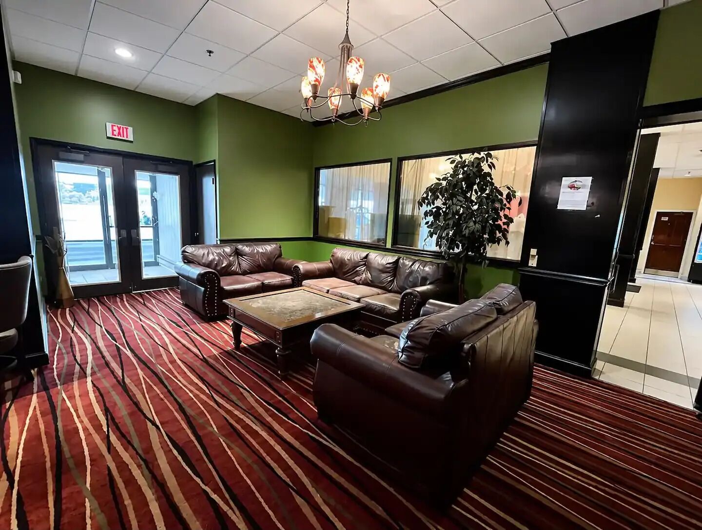 A lobby with a red carpet, leather couches, a chandelier, and an exit sign.