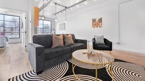 Ein modernes Interieur mit einem grauen Sofa, einem schwarzen Sessel, einem runden Couchtisch und einem schwarz-weißen Teppich.