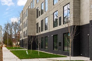 A multi-story building with a modern architectural design, featuring a combination of light and dark facade materials, large windows, and a well-maintained lawn with young trees. - Skyline Retreat | Pet Friendly + Rooftop Hot Tub (Traverse City)
