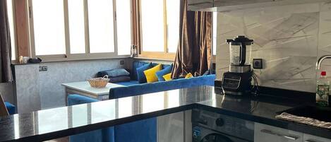 A modern kitchen with a central island, a built-in washing machine, and a dining area with blue furniture.